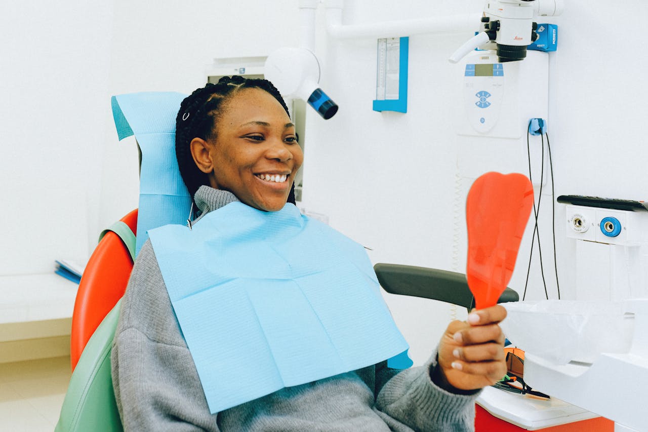 Invisible Aligners: Why Should You Go for It? Smiling woman holding a mirror during a dental check-up in a clinic.