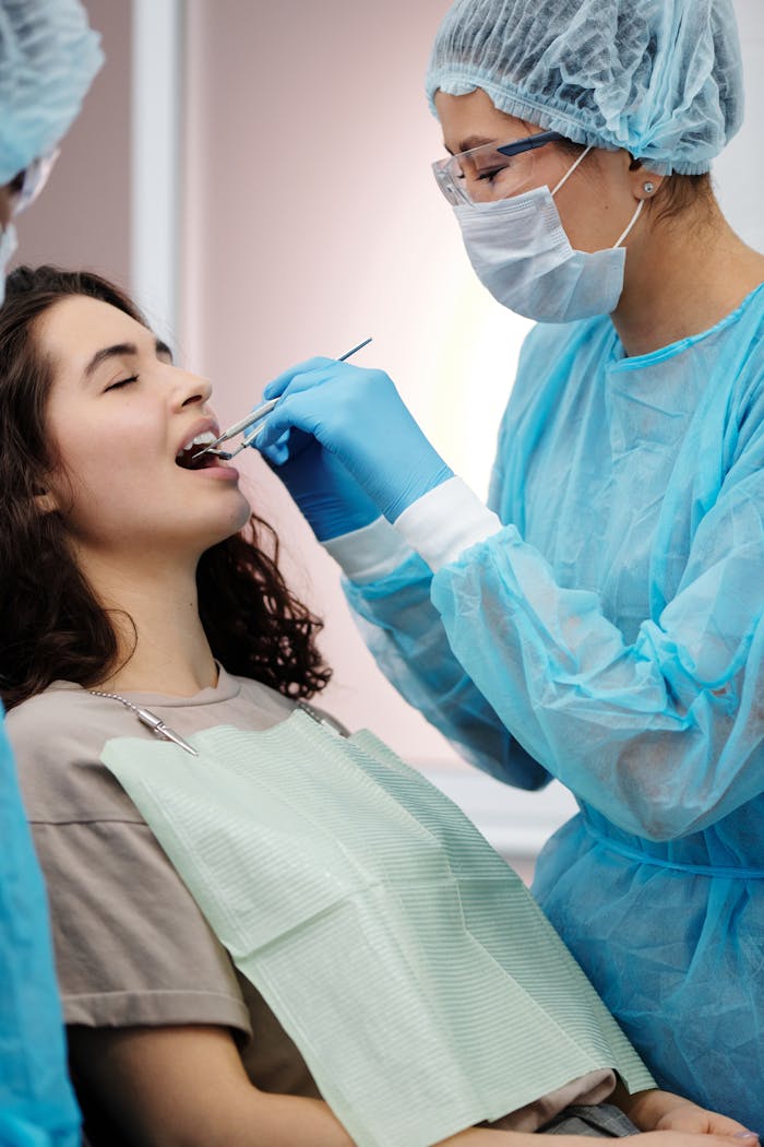 Teeth Whitening: A Brighter, More Confident Smile Dentist in protective gear examining a woman's teeth during a dental clinic visit.